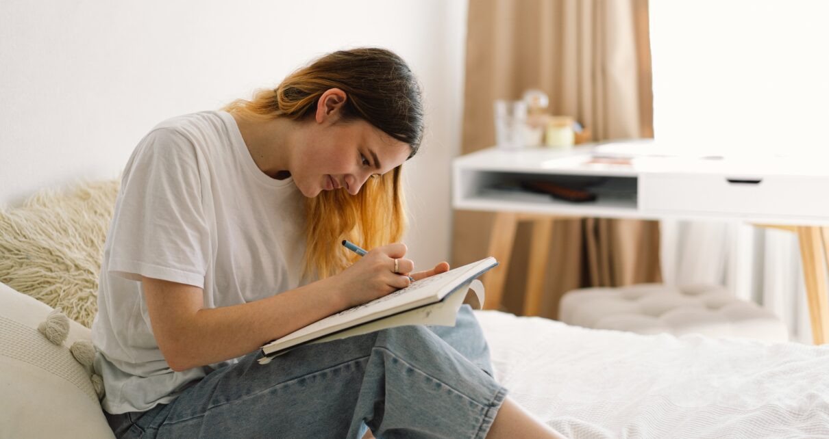 A teenage girl is drawing or doing homework in the bedroom. A teenager studies at home.