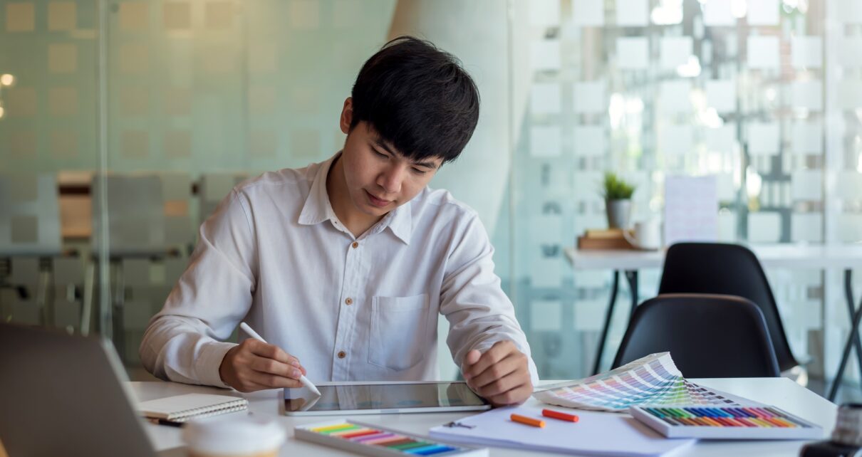 Asian man designer is drawing, creating a sample design using a color sample tablet at the office.