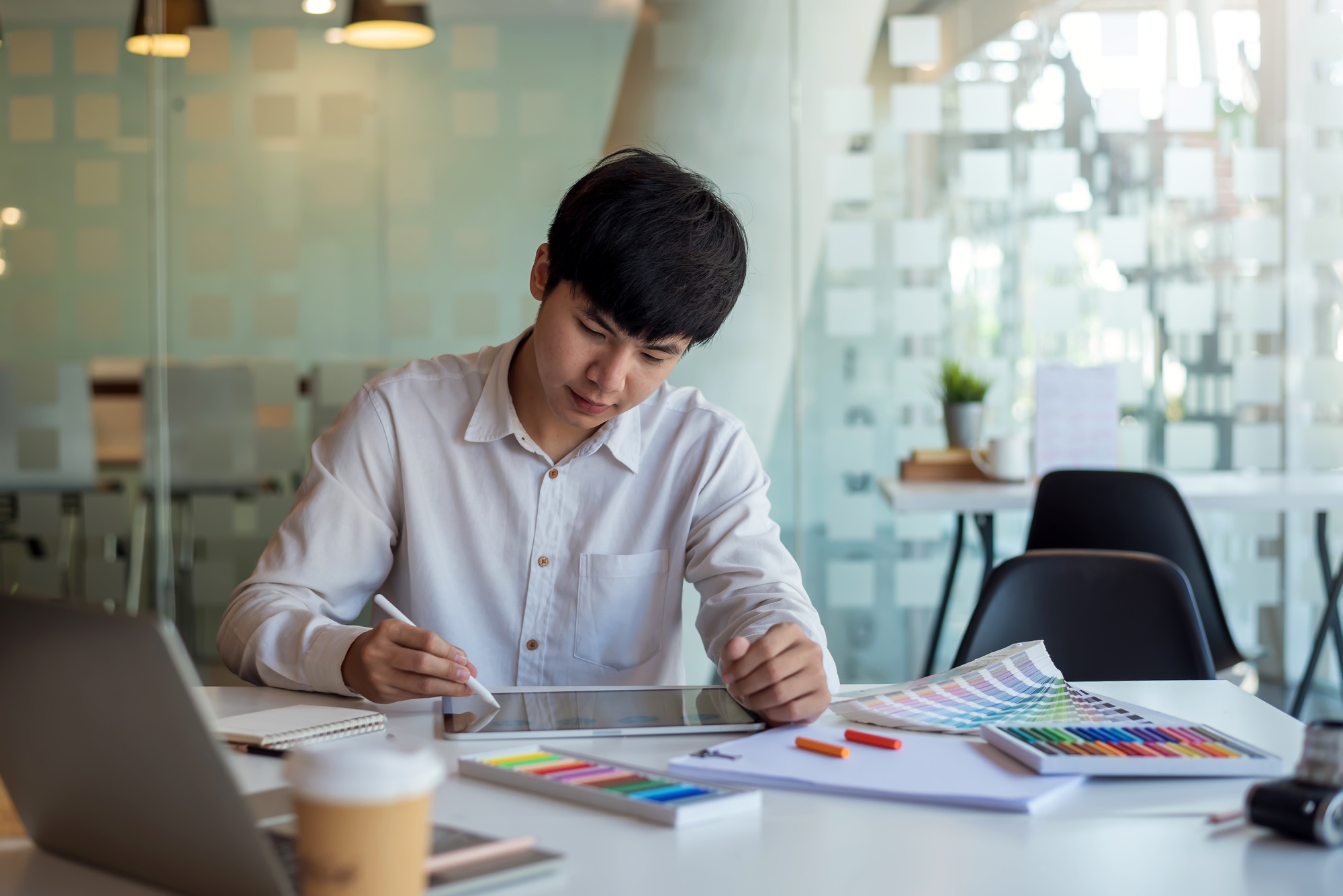 Asian man designer is drawing, creating a sample design using a color sample tablet at the office.