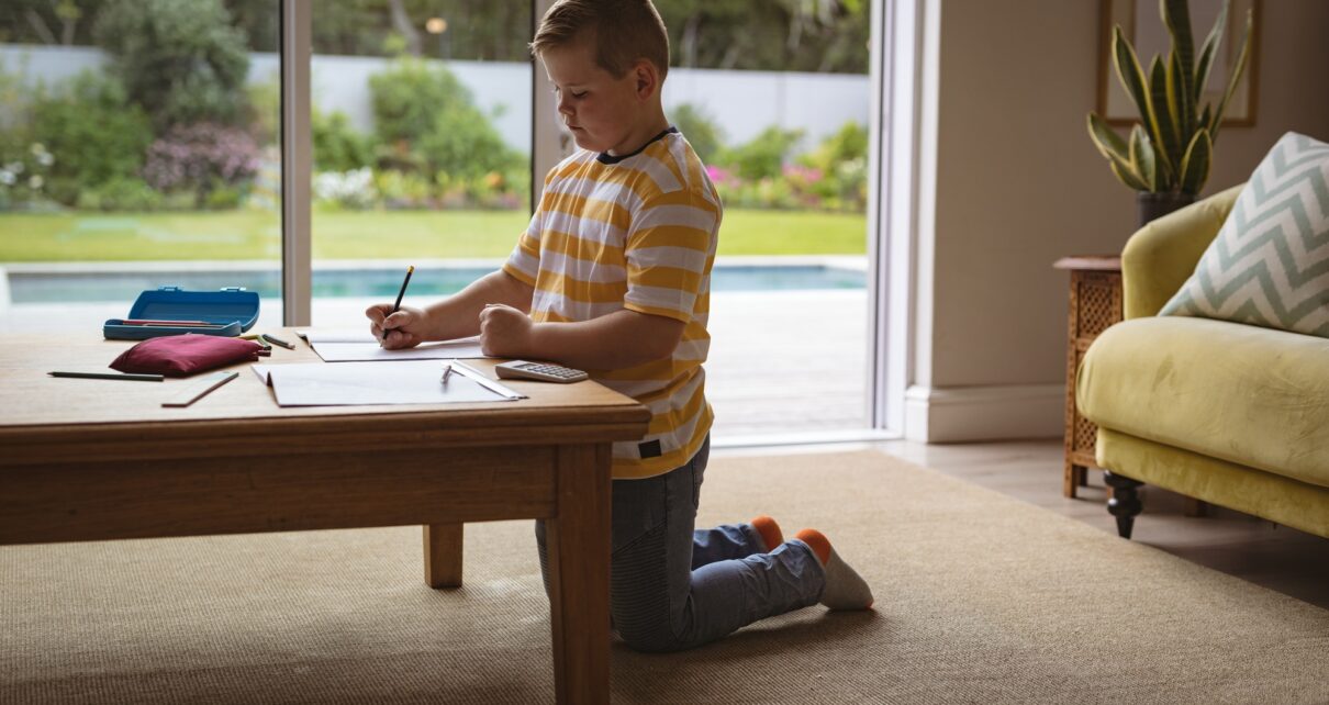 Caucasian boy drawing in his book sitting in the living room at home