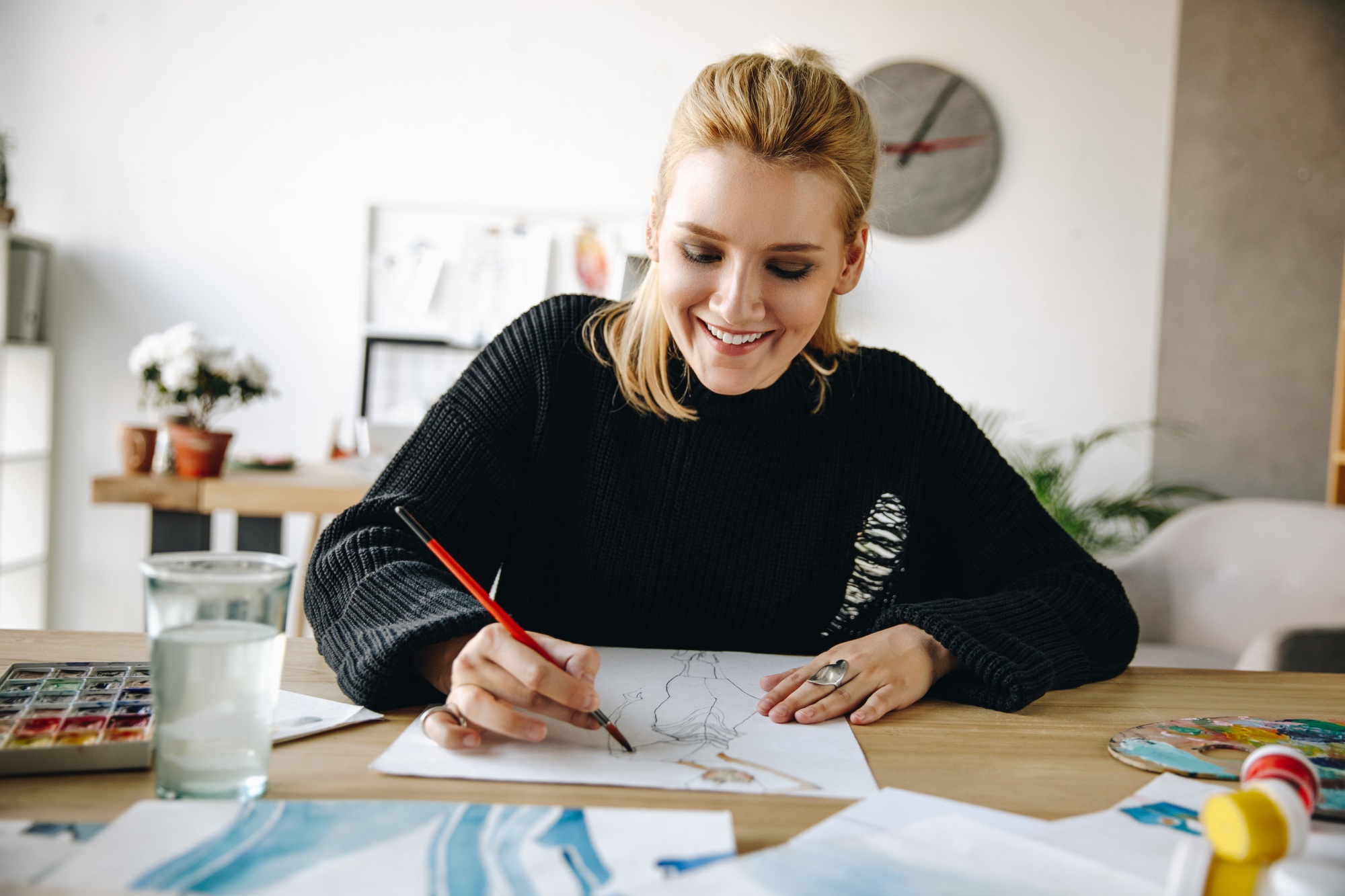 cheerful young fashion designer drawing watercolor sketch at workplace