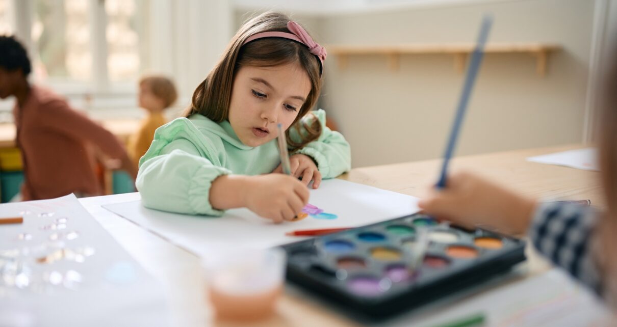 Creative girl drawing on the paper on art class at preschool.