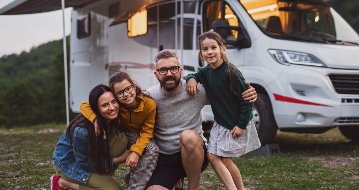 Happy family looking at camera outdoors at dusk, caravan holiday trip