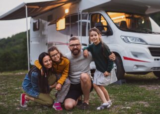 Happy family looking at camera outdoors at dusk, caravan holiday trip