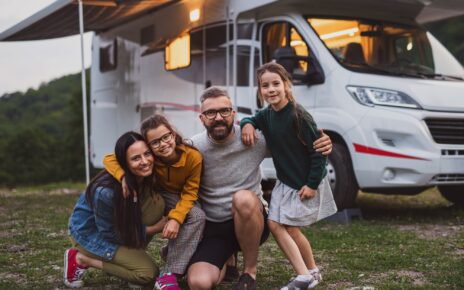 Happy family looking at camera outdoors at dusk, caravan holiday trip