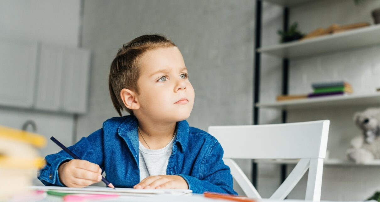 thoughtful little kid drawing with color pencils at home