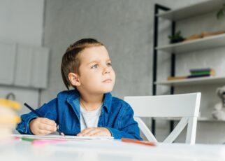 thoughtful little kid drawing with color pencils at home