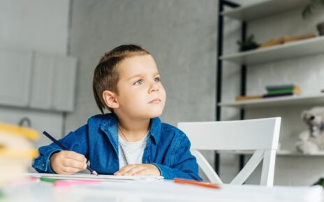 thoughtful little kid drawing with color pencils at home