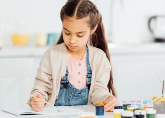 focused kid drawing with paintbrush on paper at home