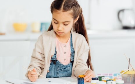 focused kid drawing with paintbrush on paper at home