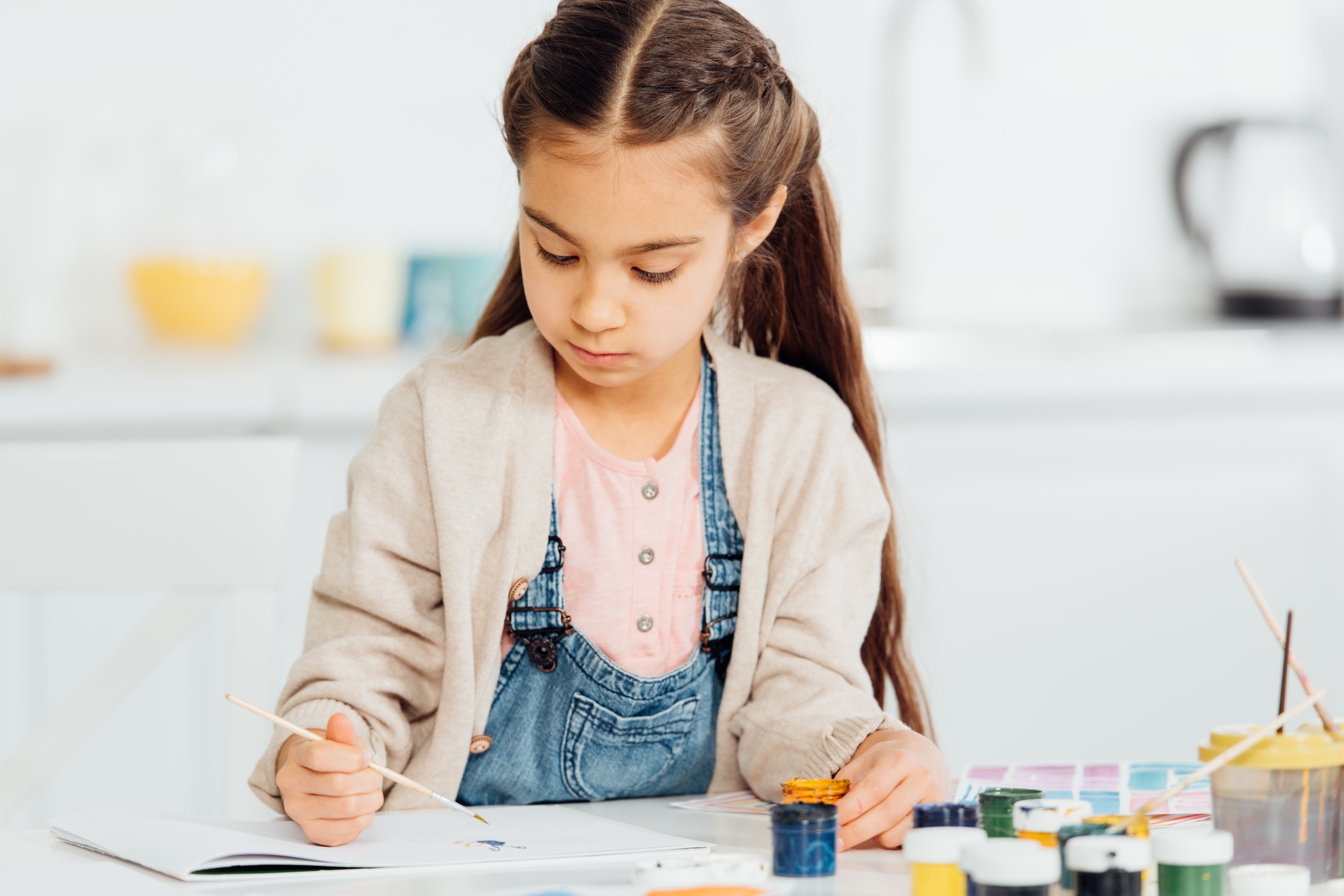 focused kid drawing with paintbrush on paper at home